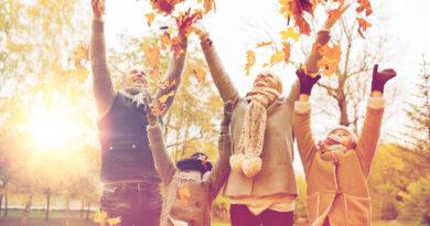 Glückliche Familie, die in warmer Kleidung mit Herbstblättern im Park spielt.