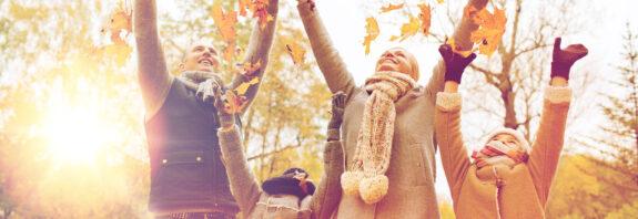 Glückliche Familie, die in warmer Kleidung mit Herbstblättern im Park spielt.